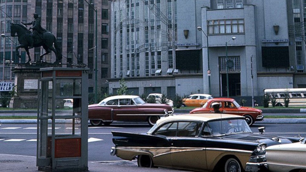 Calle con edificios y varios automóviles antiguos.