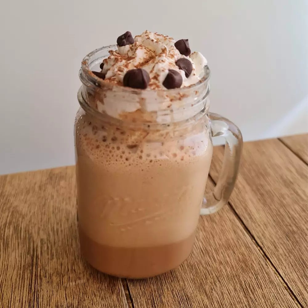 Mokaccino HERSHEY'S con crema, Mini Kisses y Cocoa en polvo, servido en un mason jar de cristal sobre una mesa de madera