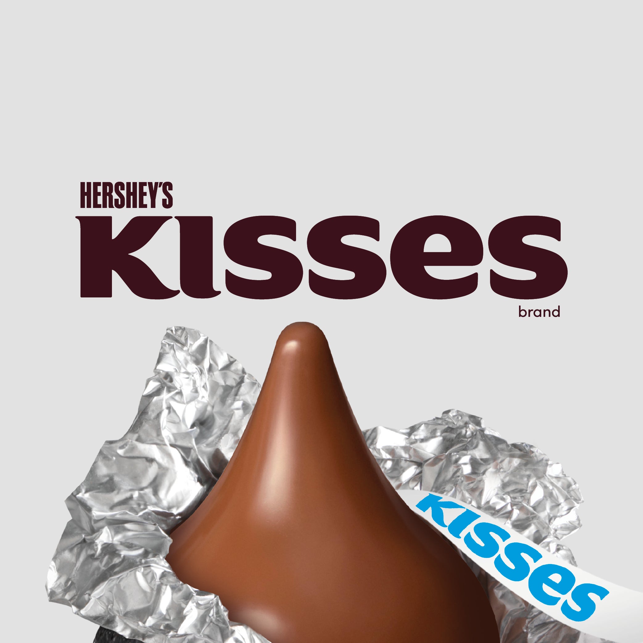Se muestra la marca HERSHEY'S KISSES, con 2 KISSES Milk al frente, uno sin envoltura y otro al frente con su envoltura de aluminio tradicional.
