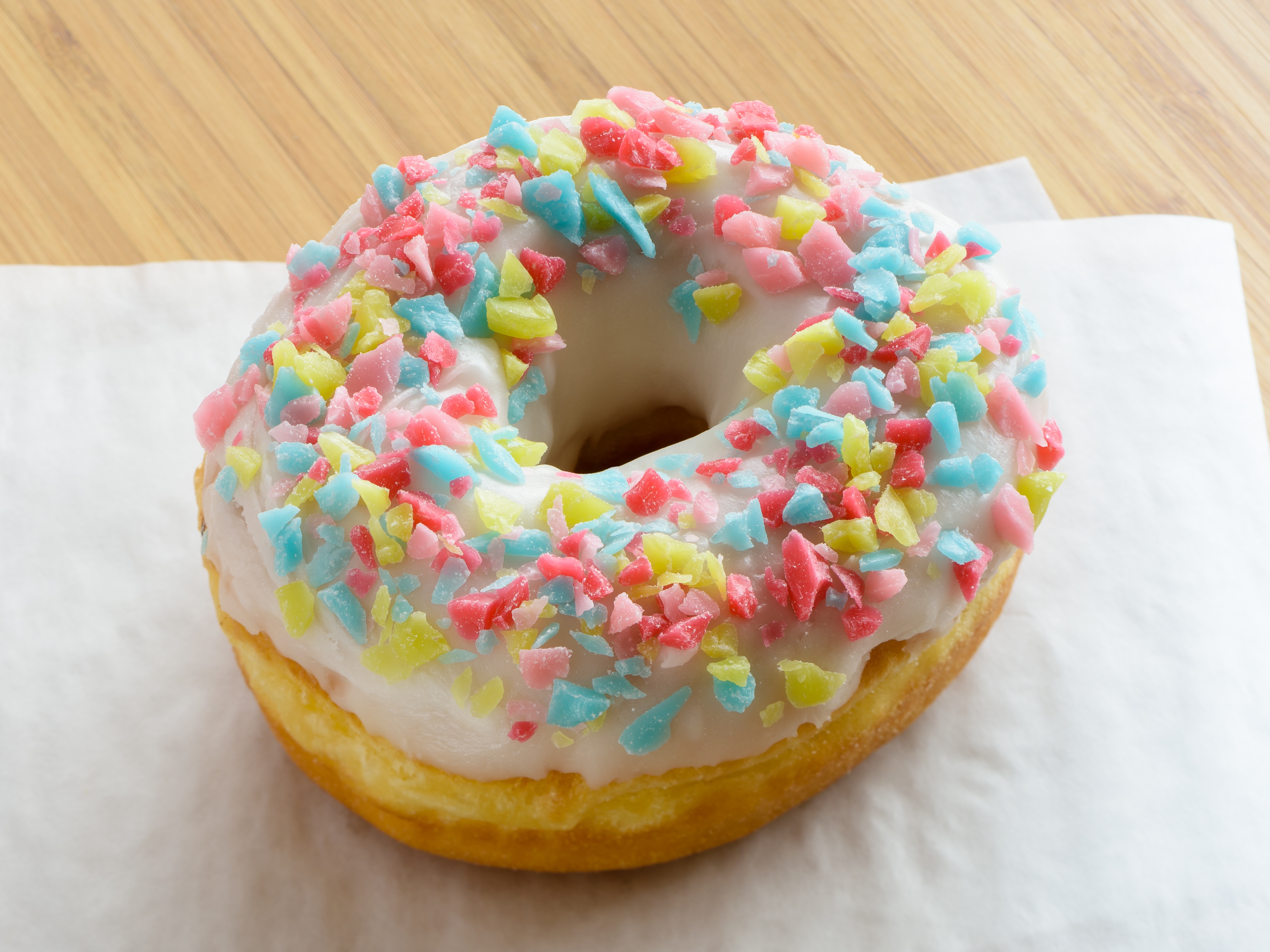 Se ve una dona con glaseado y un topping de caramelos JOLLY RANCHER de colores sobre unas servilletas blancas sobre una mesa de madera.