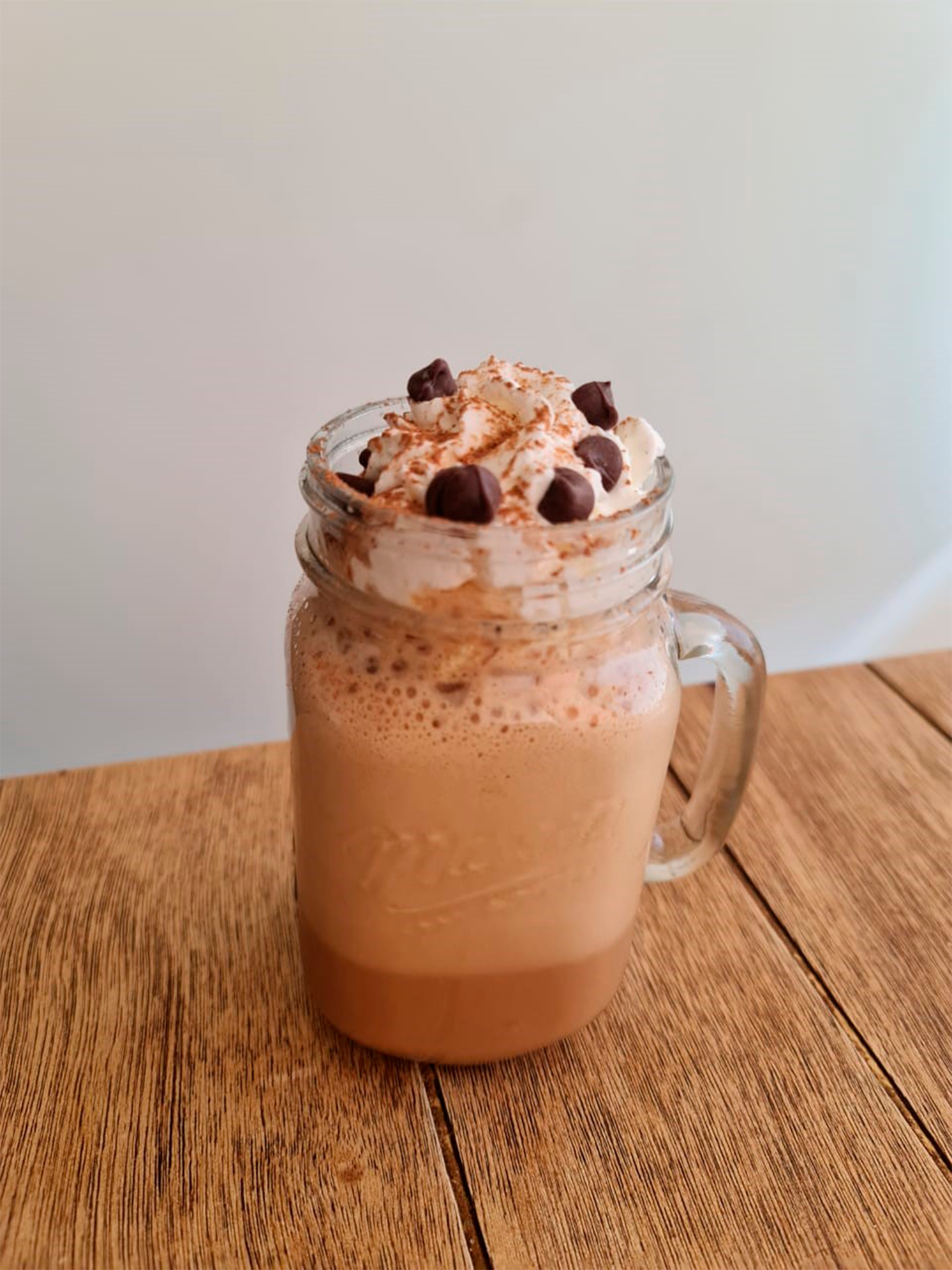 " Sobre una mesa de madera, un frasco de cristal con bebida de chocolate decorada con crema batida y chispas."