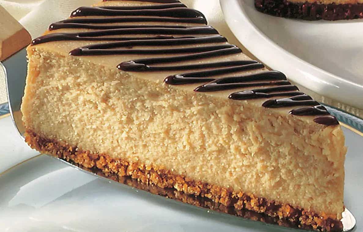 Una rebanada de cheesecake de cacahuate con base de galleta y decorado de chocolate en la parte superior. 