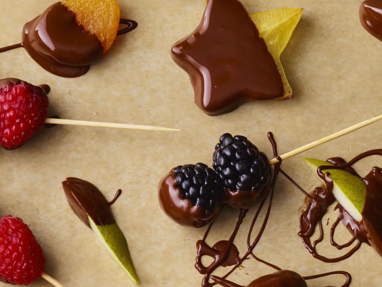 Sobre una base, brochetas de frambuesa, carambola, manzana y zarzamoras cubiertas de chocolate. 