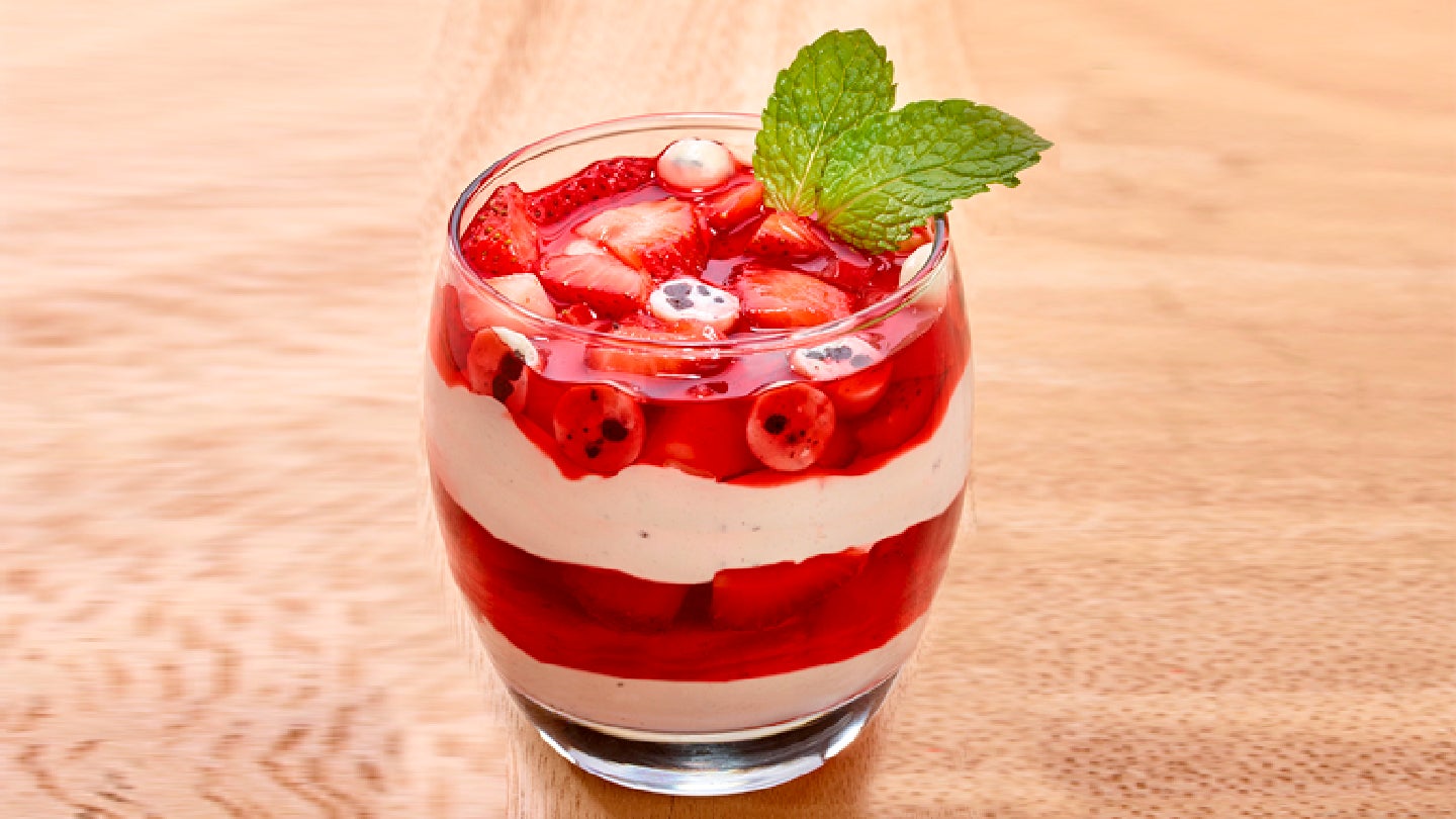 Vaso de cristal con Fresas con crema y Cookies 'n' Creme sobre mesa de madera.