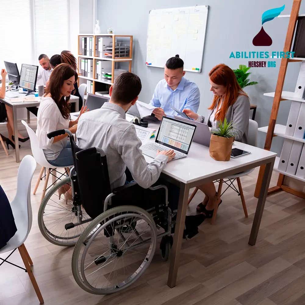 2 grupos de personas formados por mujeres y hombres trabajando en una habitación. En la esquina superior derecha se encuentra el logo de Abilities First Hershey's BRG.