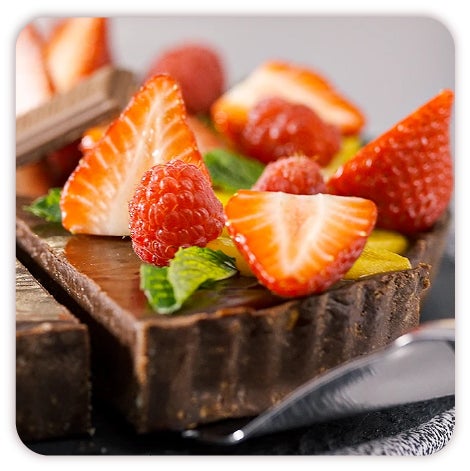 Mezcla. Sobre un fondo con textura de madera se ve una fotografía de un bowl metálico y un batidor lleno de Chocolate derretido. Al frente del bowl se alcanza a apreciar una Barra de Chocolate.