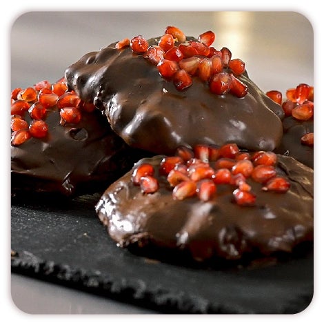 Decora.  Sobre un fondo con textura de madera se ve una fotografía de un postre de Chocolate decorado con frutos rojos, una rosa y chocolate.